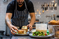 man in striped apron carefully arranging bread on plates