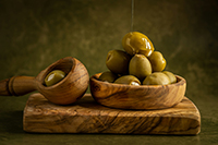 oil being poured over wooden bowl full of green olives
